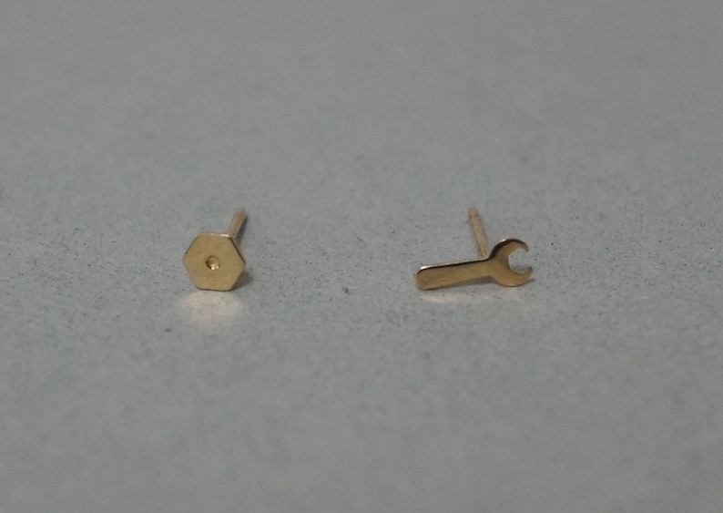 May include: A pair of gold earrings, one shaped like a hexagon and the other shaped like a wrench.