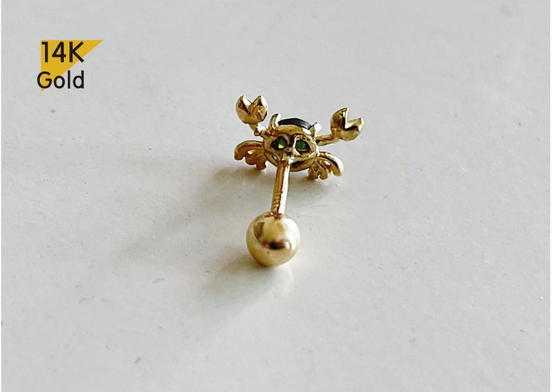 May include: 14K gold crab earring with green and black gemstones. The earring is a stud with a ball post.