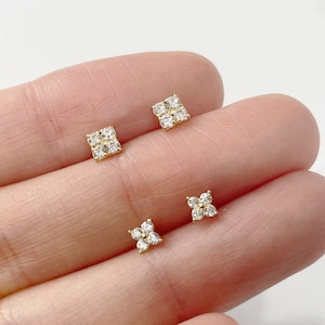 May include: A pair of gold earrings with small, clear cubic zirconia stones set in a square and a four-leaf clover shape.