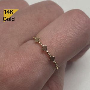 May include: A delicate gold ring with a chain of small beads and four clover-shaped charms. The ring is 14K gold.