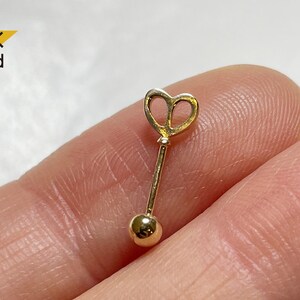 May include: 14K Gold heart-shaped key charm with a ball end. The charm is on a finger.