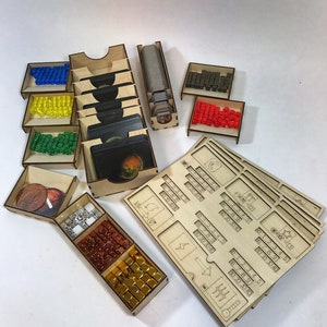 Puede incluir: Un organizador de madera para un juego de mesa con múltiples compartimentos para guardar cartas, fichas y dados. El organizador incluye un compartimento para monedas, un compartimento para cubos pequeños y un compartimento para cubos más grandes. El organizador también incluye un compartimento para cartas y un compartimento para dados. El organizador está hecho de madera y tiene un acabado natural.