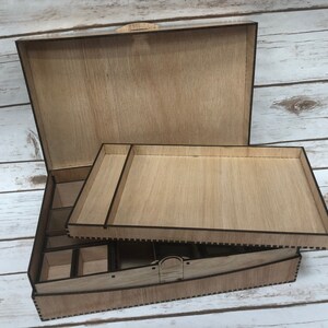 Puede incluir: Una caja de madera con tapa abatible y una bandeja extra&iacute;ble. La caja tiene un acabado de madera natural y est&aacute; dividida en compartimentos. La bandeja tambi&eacute;n est&aacute; hecha de madera y tiene una superficie lisa.