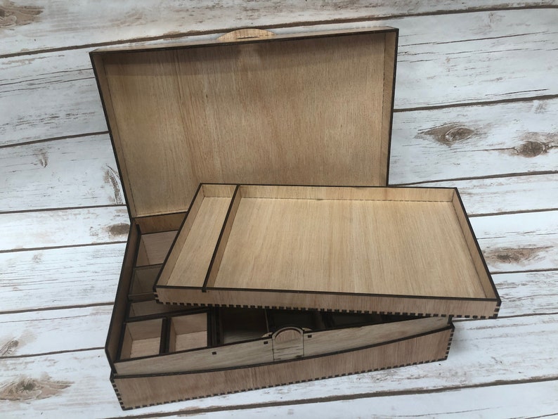 Puede incluir: Una caja de madera con tapa abatible y una bandeja extra&iacute;ble. La caja tiene un acabado de madera natural y est&aacute; dividida en compartimentos. La bandeja tambi&eacute;n est&aacute; hecha de madera y tiene una superficie lisa.