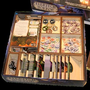 以下が含まれることがあります： ボードゲーム「エルドリッチホラー」用の木製オーガナイザー。オーガナイザーには、カード、トークン、サイコロ、ゲームピース用の複数のコンパートメントがあります。ゲームボックスとルールブックも表示されています。
