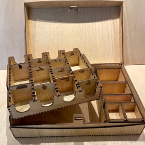 Puede incluir: Una caja de madera con tapa y varios compartimentos para organizar las piezas de juego. La caja est&aacute; hecha de madera marr&oacute;n claro y tiene un acabado natural.