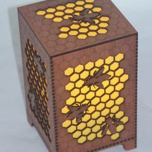 May include: A wooden lamp with a honeycomb design and bees cut out. The lamp is lit from the inside, casting a warm glow.