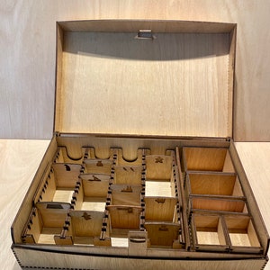 Puede incluir: Una caja de madera con tapa abatible y m&uacute;ltiples compartimentos para organizar piezas de juego. La caja est&aacute; hecha de madera marr&oacute;n claro y tiene un acabado natural.