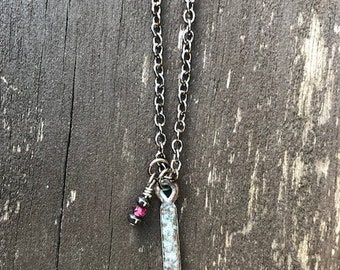 May include: A silver chain necklace with a long, rectangular pendant and a small pink gemstone charm.