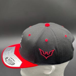 May include: A black and red baseball cap with a red embroidered bat logo on the front. The cap has a black brim and a red underside.