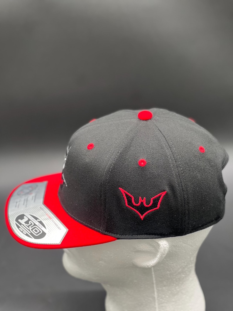 May include: A black and red baseball cap with a red embroidered bat logo on the front. The cap has a black brim and a red underside.