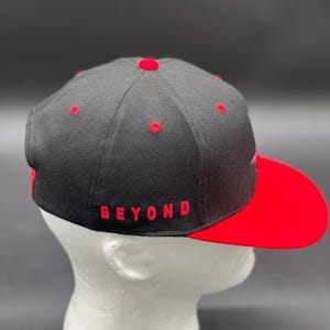 May include: A black and red baseball cap with a red brim and the word "BEYOND" embroidered in red on the front.