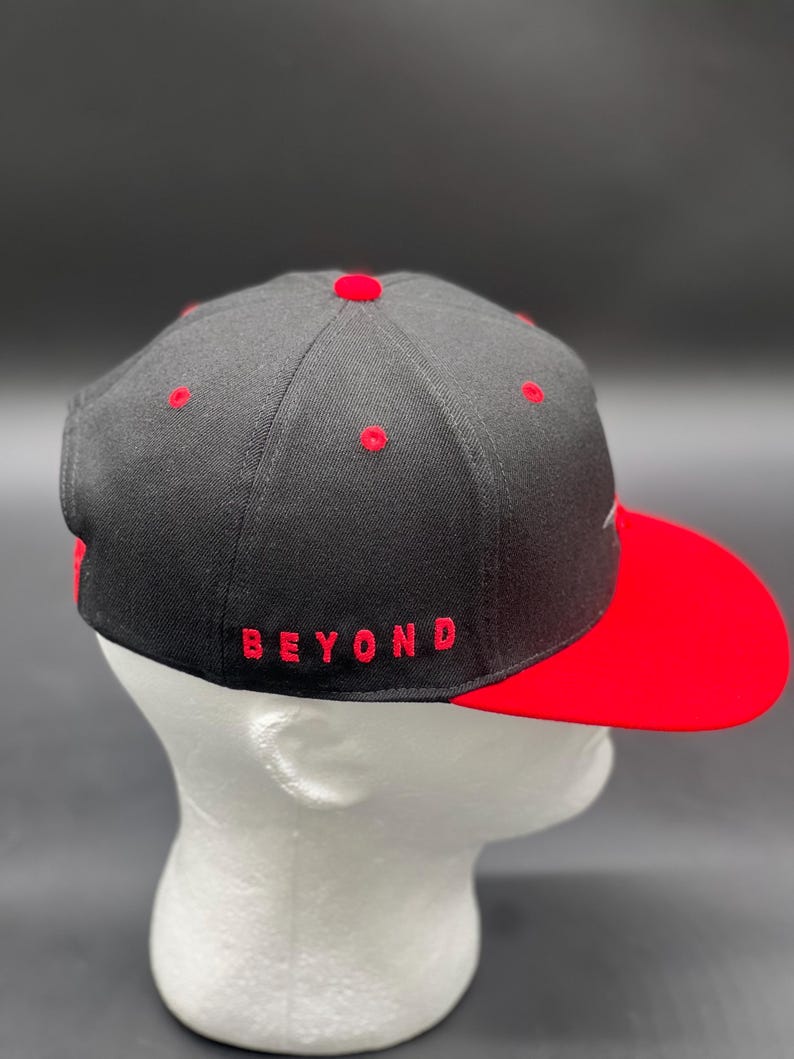 May include: A black and red baseball cap with a red brim and the word "BEYOND" embroidered in red on the front.