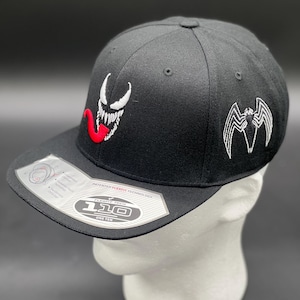 May include: Black baseball cap with a white embroidered Venom logo on the front and a white embroidered Venom symbol on the back. The cap has a black Flexfit 110 logo on the side.