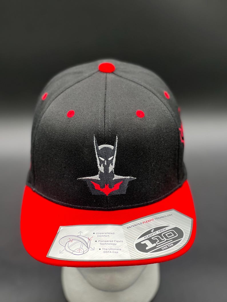 May include: Black and red baseball cap with a black embroidered Batman logo. The cap features Flexfit technology and the text "110 One Ten".