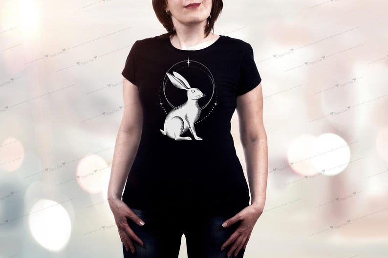 May include: Black t-shirt featuring a detailed illustration of a white rabbit within a circular design. The rabbit is depicted in a seated position, with long ears and a serene expression. The design is centered on the shirt, creating a striking visual.