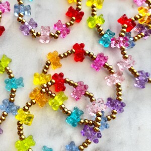 May include: A set of colorful gummy bear bracelets with gold beads. The bracelets are made with small, clear gummy bears in a variety of colors, including red, orange, yellow, green, blue, purple, and pink. The bracelets are strung on gold beads and are perfect for adding a fun and playful touch to any outfit.