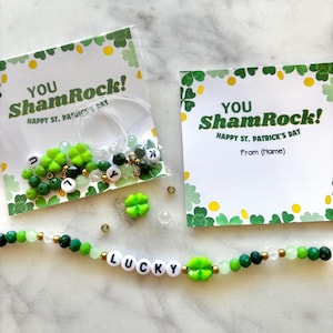 May include: A green and white card with the text "You ShamRock! Happy St. Patrick's Day" and a green and white bracelet with the word "LUCKY" spelled out in white beads.