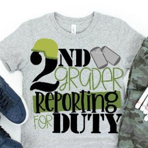 Puede incluir: Una camiseta gris con un dise&ntilde;o en negro y verde que dice "2nd Grader Reporting for Duty". El dise&ntilde;o incluye un casco verde del ej&eacute;rcito y dos chapas de identificaci&oacute;n verdes. La camiseta se combina con pantalones de camuflaje y zapatillas azules.