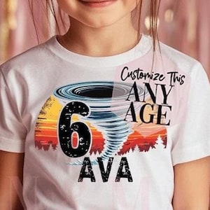 Puede incluir: Una niña lleva una camiseta blanca con un gráfico colorido de un tornado, el número 6 y el nombre AVA. La camiseta también tiene el texto "Customize This ANY AGE". El fondo incluye globos rosas y blancos.