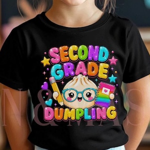 May include: A black t-shirt featuring a colourful graphic of a cartoon dumpling wearing glasses, holding a pencil and a notebook. The text reads SECOND GRADE DUMPLING in bright, multi-coloured letters, surrounded by small stars and hearts.