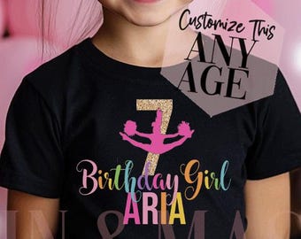 Può includere: Una t-shirt nera a maniche corte con un numero sette glitterato oro, una grafica rosa da cheerleader e il testo Birthday Girl ARIA in lettere colorate. Una sovrapposizione semitrasparente mostra il testo Customize This ANY AGE.