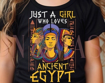 May include: A young girl wearing a black t-shirt with a graphic design of three women with Egyptian headdresses. The text on the shirt reads "Just a girl who loves Ancient Egypt".