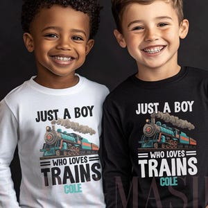 May include: Two boys wearing long-sleeved shirts with a train graphic. The shirts read "JUST A BOY WHO LOVES TRAINS" with the name "COLE" below the text. One shirt is white, the other is black.