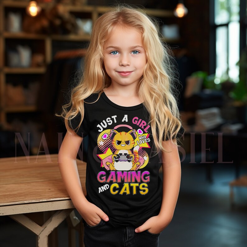 May include: Black t-shirt with a cartoon cat graphic wearing headphones and holding a game controller. The text reads "JUST A GIRL WHO LOVES GAMING AND CATS" in pink and white. The cat is orange and white.