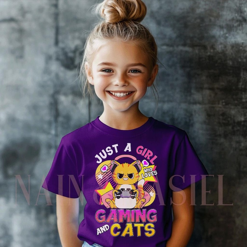 May include: A purple t-shirt featuring the text "JUST A GIRL WHO LOVES GAMING AND CATS" and a cartoon cat playing a video game. The cat is orange and yellow with headphones. The shirt is worn by a young girl.