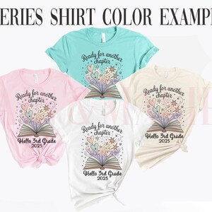Puede incluir: Una colecci&oacute;n de camisetas en varios colores, incluyendo rosa, turquesa, blanco y crema. Cada camiseta presenta un gr&aacute;fico de un libro abierto con corazones, estrellas y el texto "Ready for another chapter" y "Hello 3rd Grade 2025".