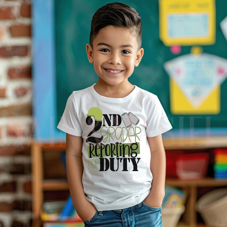 Puede incluir: Una camiseta blanca con un gr&aacute;fico verde y negro que dice "2nd Grader Reporting for Duty". El gr&aacute;fico incluye un casco militar y placas de identificaci&oacute;n.