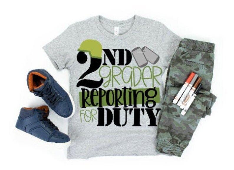 Puede incluir: Una camiseta gris con un dise&ntilde;o en negro y verde que dice "2nd Grader Reporting for Duty". El dise&ntilde;o incluye un casco verde del ej&eacute;rcito y dos chapas de identificaci&oacute;n verdes. La camiseta se combina con pantalones de camuflaje y zapatillas azules.