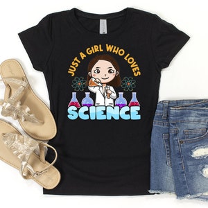 May include: Black t-shirt with a cartoon illustration of a girl wearing a lab coat and holding a beaker. The text "Just a girl who loves science" is printed in yellow and blue on the shirt.