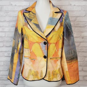 Könnte beinhalten: Ein langärmeliger Blazer mit abstraktem Aquarellmuster in Gelb-, Orange-, Blau- und Violetttönen. Das Kleidungsstück verfügt über ein steigendes Revers, zwei schwarze Knöpfe zum Schließen und eine schwarze Paspelierung an den Kanten und Taschen.