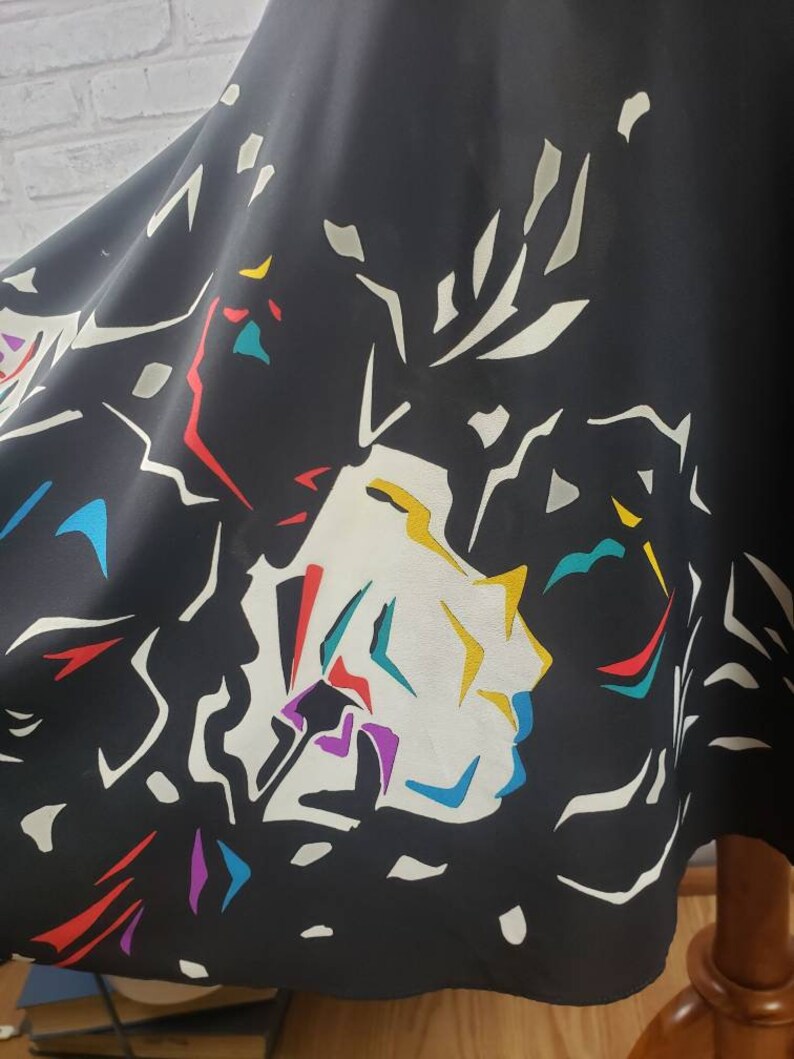 May include: Black skirt with a colorful abstract floral print. The print features white, yellow, red, blue, purple, and teal colors.