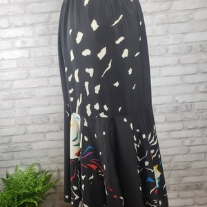 May include: A black midi skirt with a white and colorful abstract print. The skirt has a gathered hem and an elastic waistband.