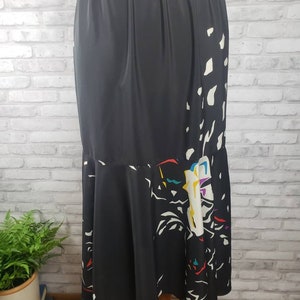 May include: A black maxi skirt with a white and colorful abstract print. The skirt has an elastic waistband and a flowing, A-line silhouette.