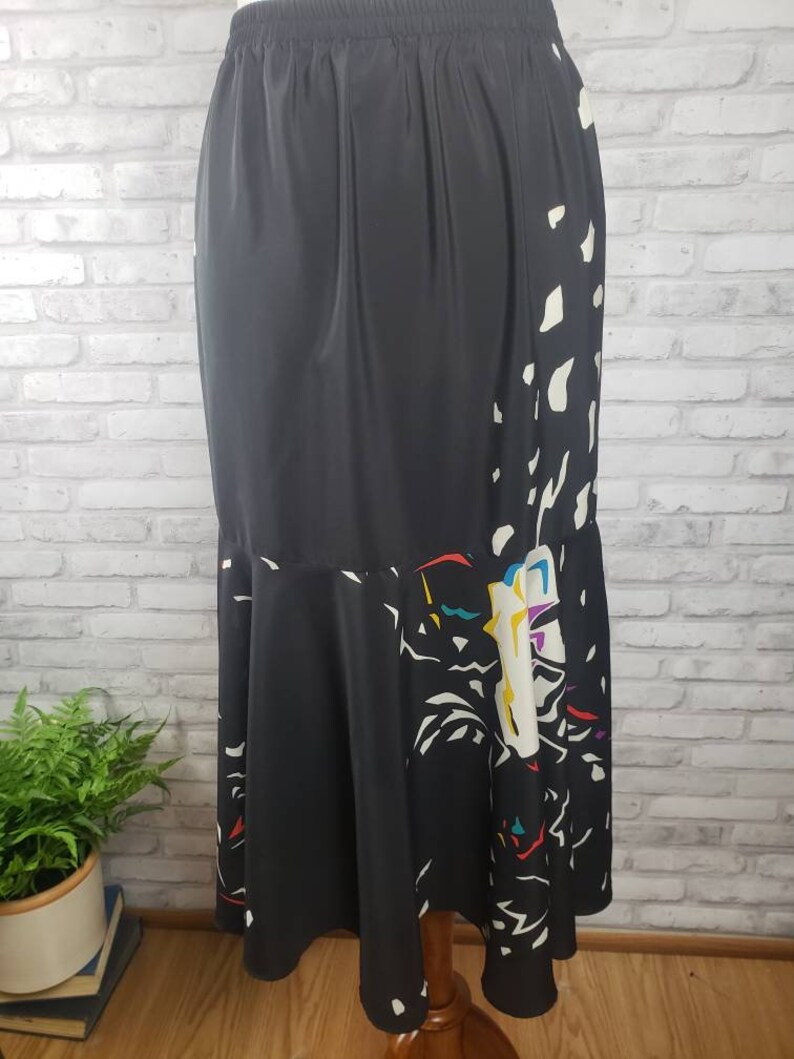May include: A black maxi skirt with a white and colorful abstract print. The skirt has an elastic waistband and a flowing, A-line silhouette.