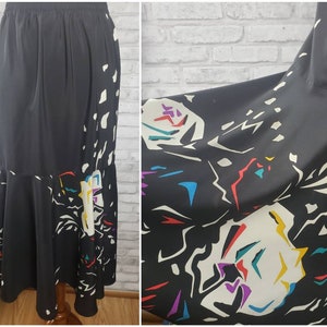 May include: A black maxi skirt with a colorful abstract print. The skirt has a flared hem and a high waist.