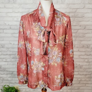 May include: A long-sleeved, red floral print blouse with a large bow tie at the neck. The blouse has a button-up front and a sheer fabric.