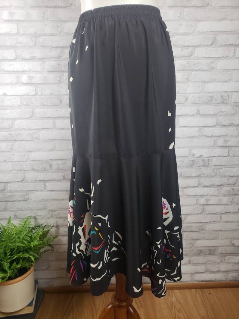 May include: A black midi skirt with a white and colorful abstract print. The skirt has a gathered waistband and a flared hem.