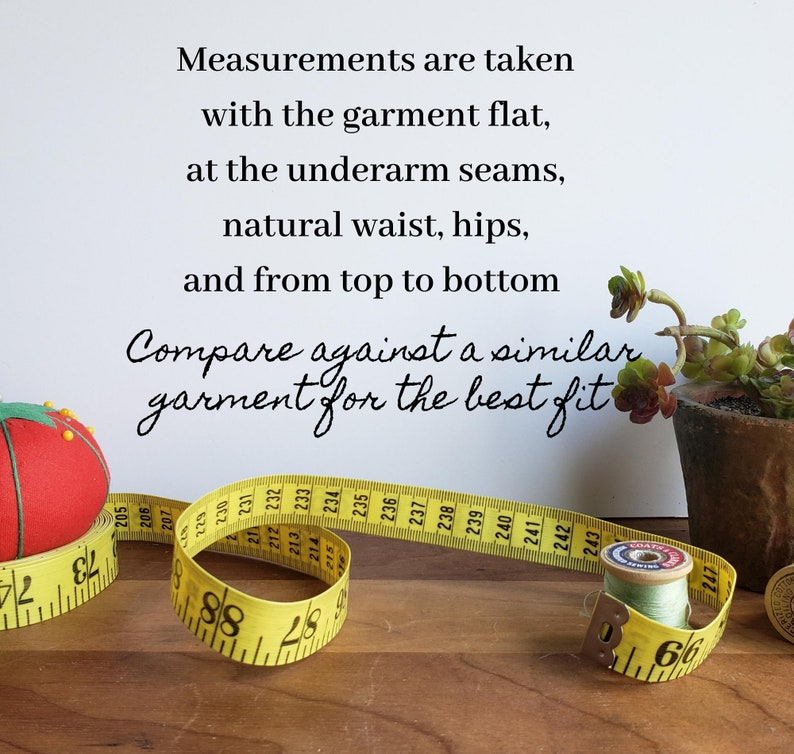 May include: Yellow measuring tape with black markings, a red pincushion in the shape of a tomato, and a spool of thread. The tape reads "Measurements are taken with the garment flat, at the underarm seams, natural waist, hips, and from top to bottom. Compare against a similar garment for the best fit."