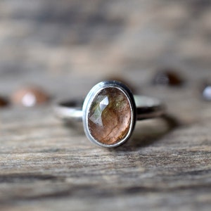 May include: A silver ring with a light brown oval gemstone set in a bezel setting.
