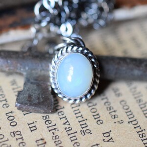 May include: A silver chain necklace with a pendant featuring a white opal stone set in a silver rope-like border.