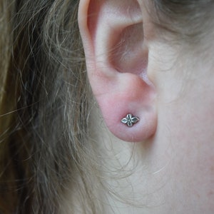 May include: A close-up of a person's ear with a small silver flower-shaped earring.