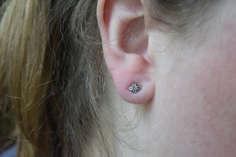 May include: A close-up of a person's ear with a small silver flower-shaped earring.