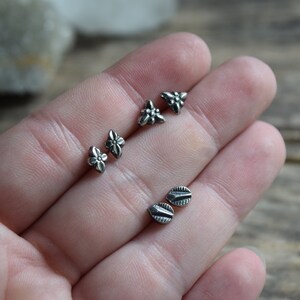 May include: Four pairs of silver stud earrings with different designs. Two pairs feature a flower design, and the other two pairs feature a leaf design.