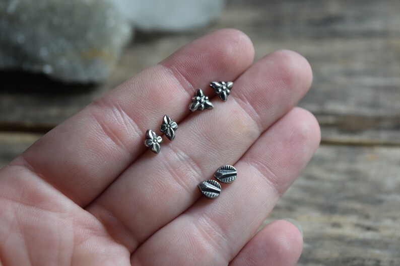May include: Four pairs of silver stud earrings with different designs. Two pairs feature a flower design, and the other two pairs feature a leaf design.