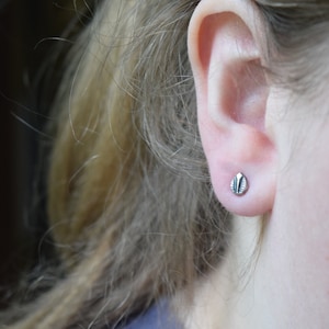 May include: A close-up of a person's ear with a small, silver stud earring. The earring has a textured, leaf-like design.